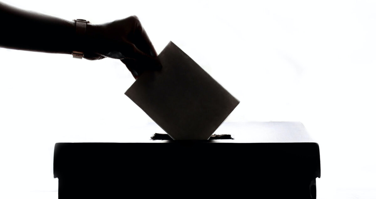 Mustavalkoinen kuva, jossa käsi laittaa äänestyslippua uurnaan.