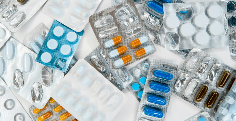 Eri värisiä tabletteja lääkeliuskoissa valkoisella pöydällä.